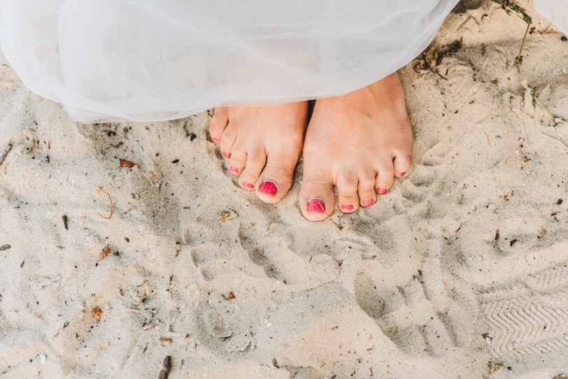 close up of feet with red pedicure standing in the sand
