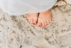 person with red pedicure standing on white textile