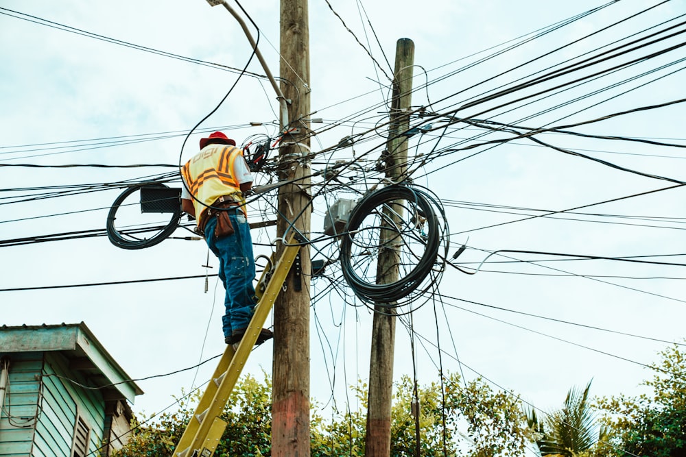 man in blue jacket and orange helmet climbing on brown wooden ladder during daytime