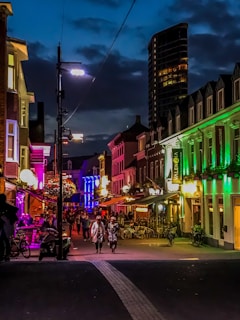 A vibrant street scene in Venus District at dusk, neon lights glowing against concrete buildings.