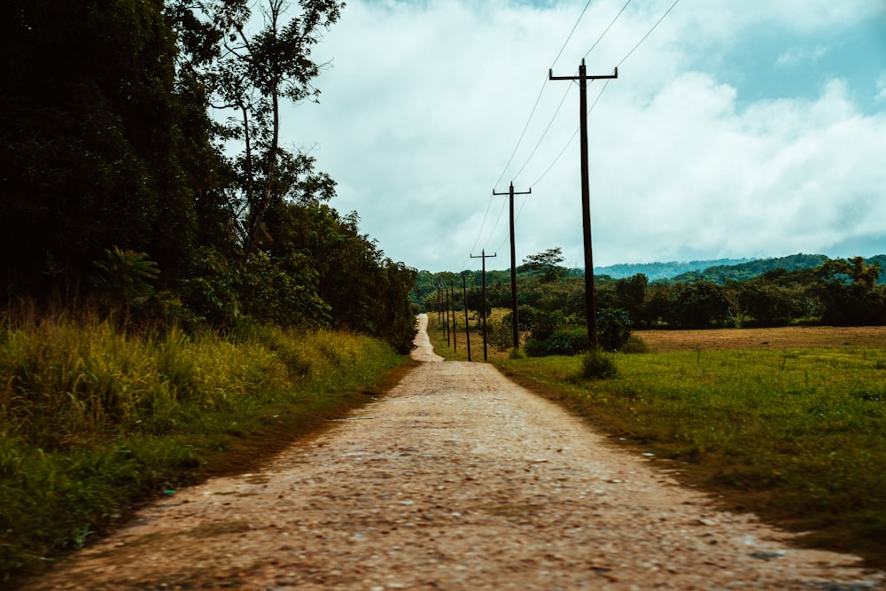 brown dirt road between green grass field under white clouds and blue sky during daytime