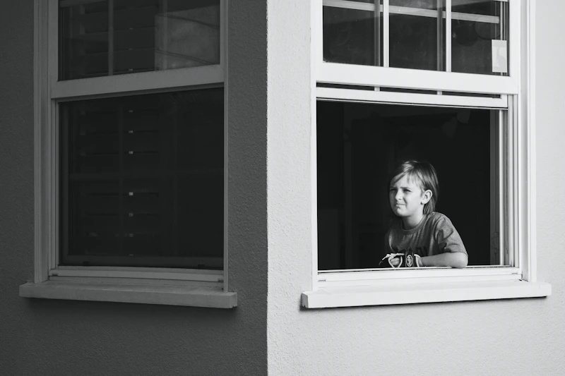 Child looking out through a window, withdrawn and contemplative