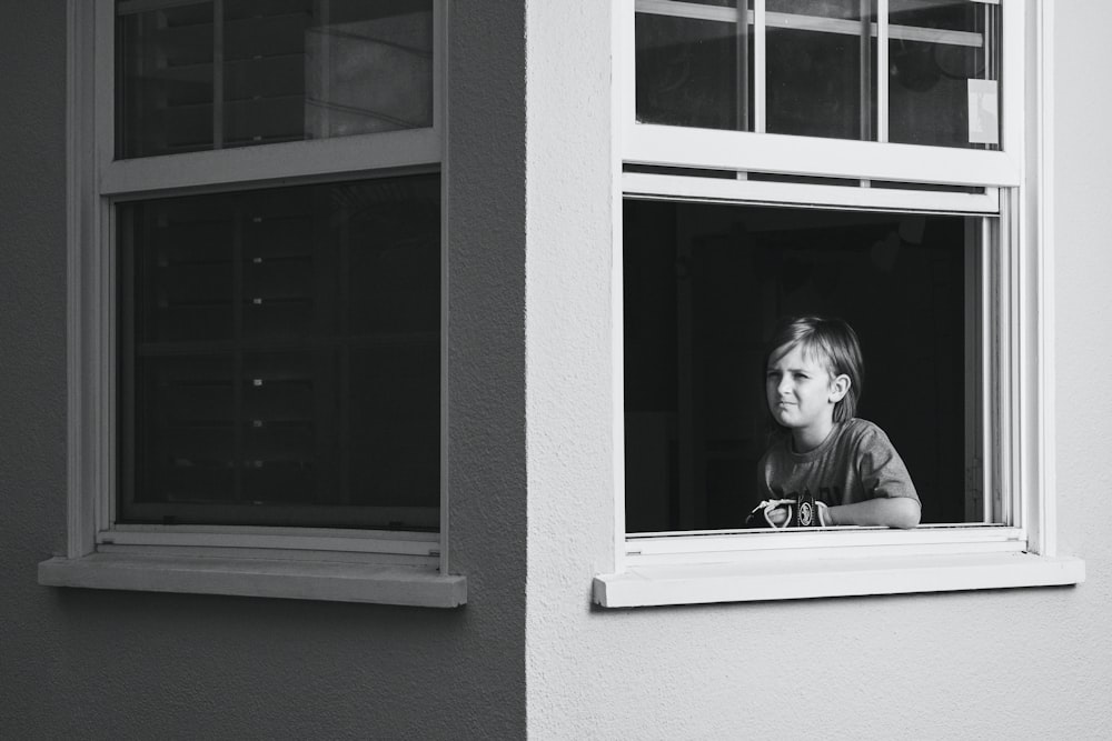 grayscale photo of girl in jacket looking out the window