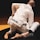 Two individuals are engaged in a jiu-jitsu match, wearing white gis. One person's back is prominently visible, showing an embroidered design and the phrase 'We Are All One.' The lighting is subdued, focusing on the competitors.