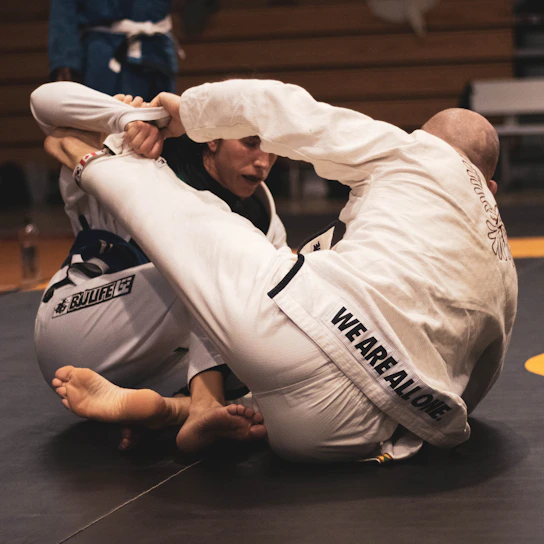 Close-up of a male BJJ athlete gripping his opponent's gi during an intense training session in a dimly lit gym.
