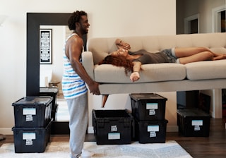 woman in white tank top and blue denim jeans sitting on brown sofa