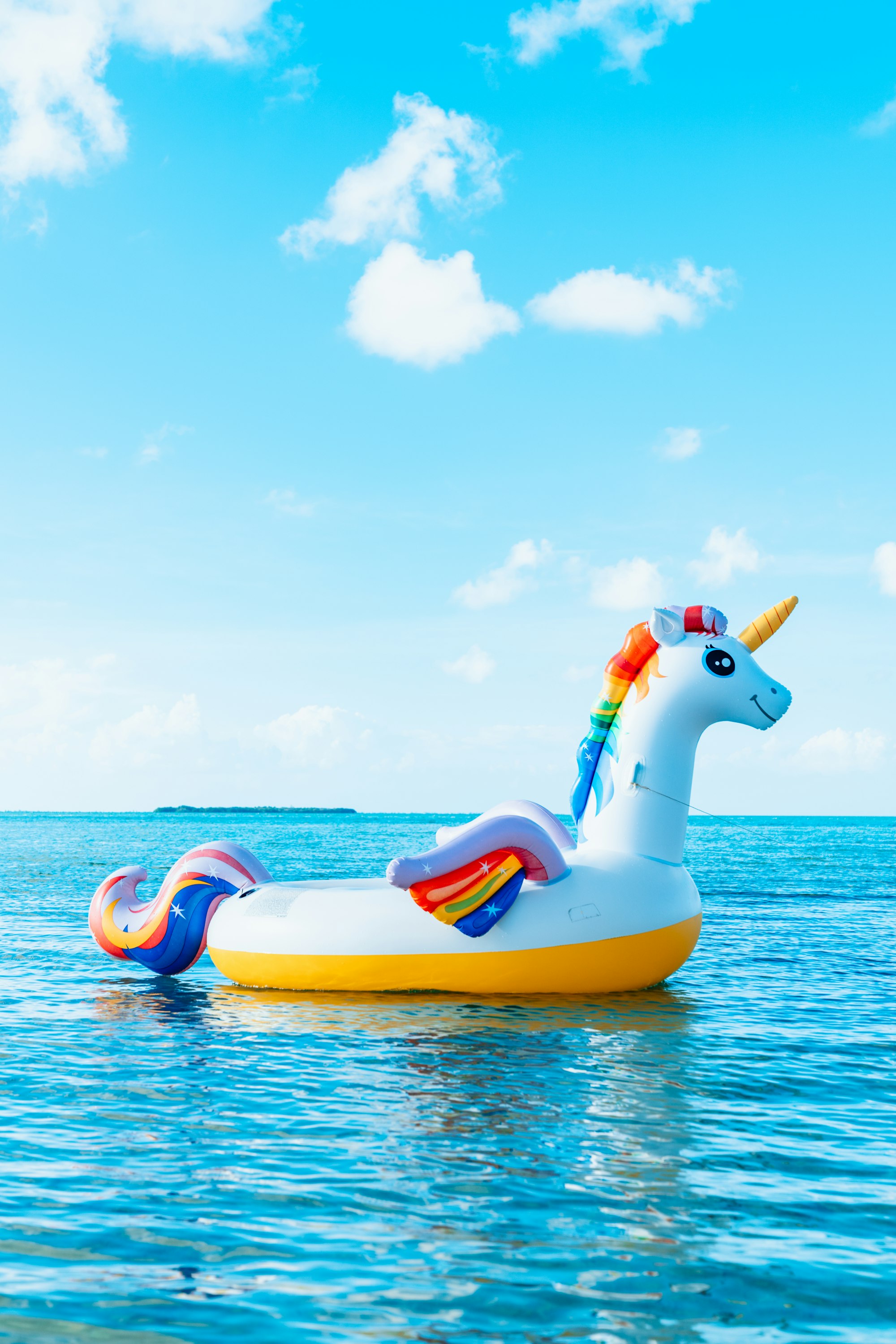 Rainbow unicorn inflatable inner tube in tropical island ocean water.