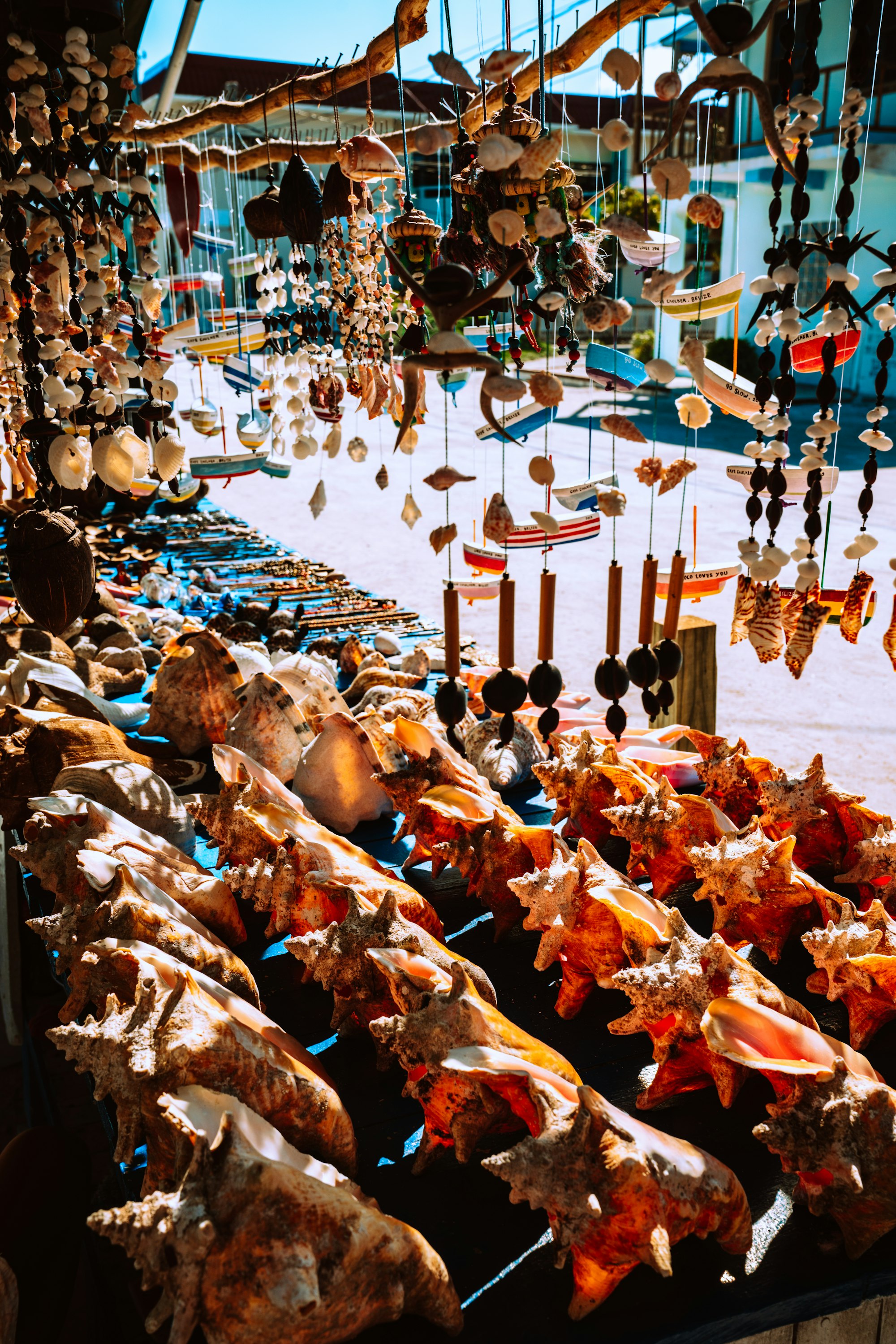 Wind chimes, conch shells, and handmade gifts for sale in a market stall.