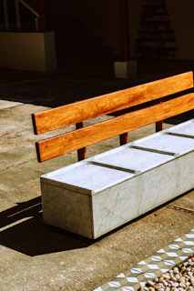 A cozy wooden bench stool with a smooth finish set against a sunlit outdoor patio.