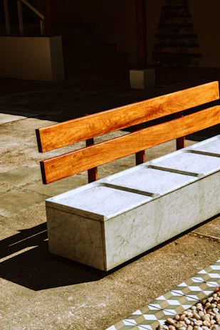 A cozy wooden bench stool with a smooth finish set against a sunlit outdoor patio.