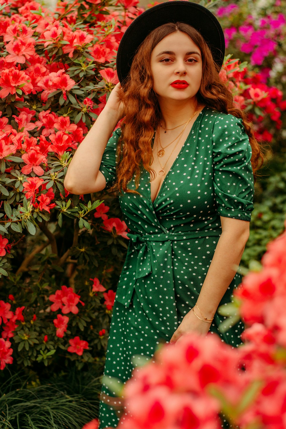 a woman in a green dress and black hat standing in front of red flowers