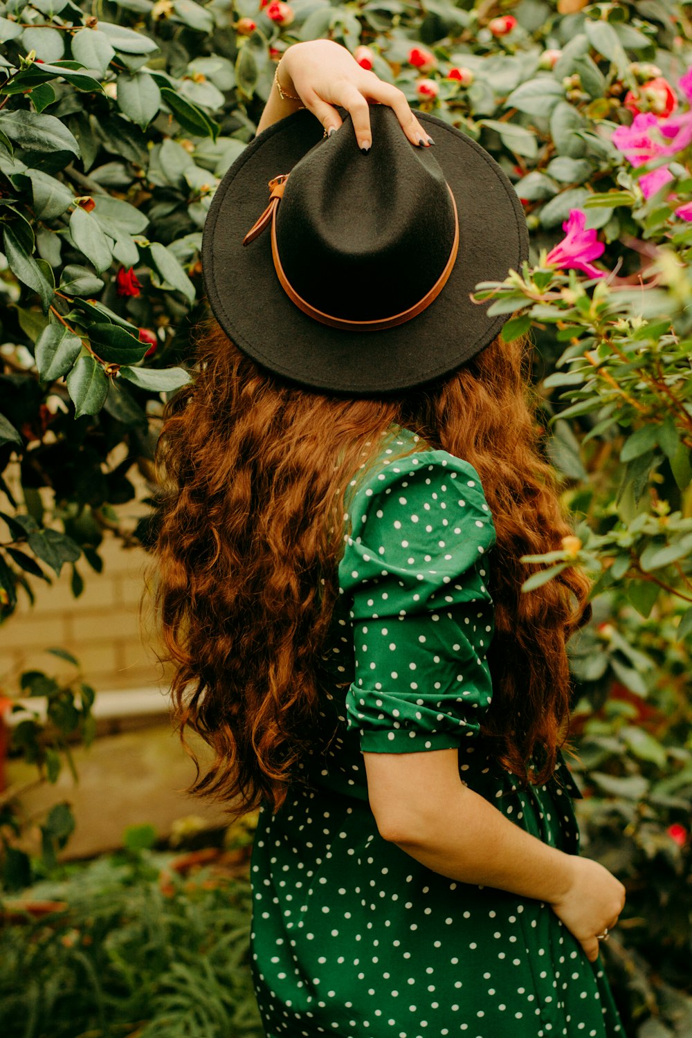 woman in black hat and green long sleeve shirt standing near red flowers