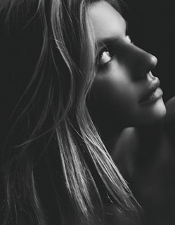 A striking black-and-white portrait capturing a thoughtful gaze against a soft charcoal grey background.