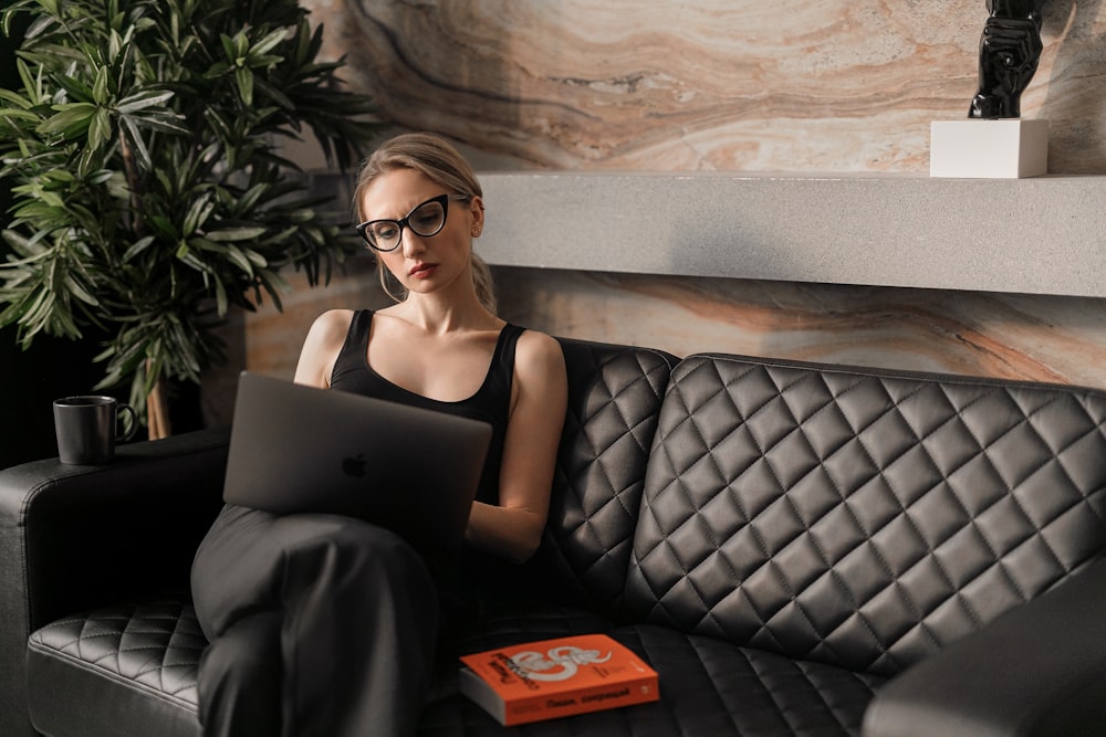 Frau in schwarzem Tanktop mit Sonnenbrille sitzt auf schwarzer Ledercouch