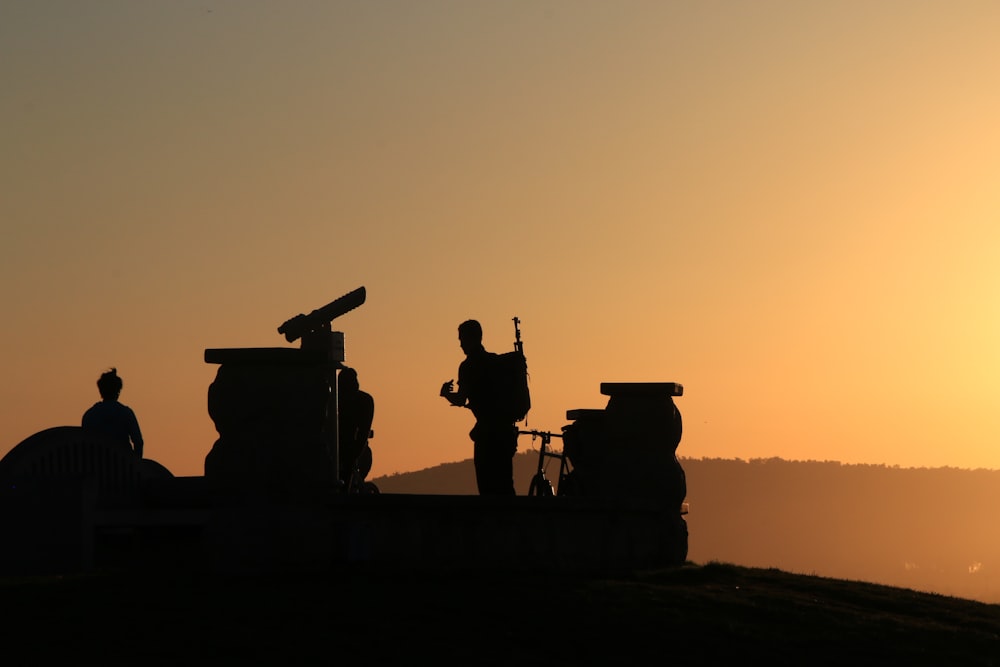 silhouette of 2 people standing on top of building during sunset