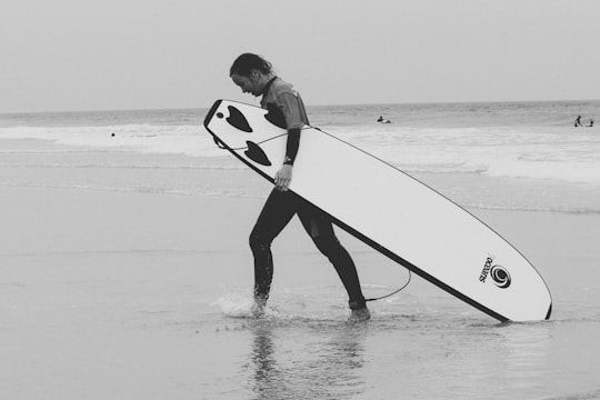 man in black wet suit holding white surfboard walking on beach during daytime in Bordeaux France