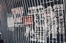 A series of vintage-style posters on a corrugated metal surface promoting a music and BBQ festival. The posters feature bold text with phrases like 'Meat Music Mayhem' and 'Grillstock BBQ & Music Festival 2014'. There is a cartoon pig character playing a guitar on the rightmost poster.
