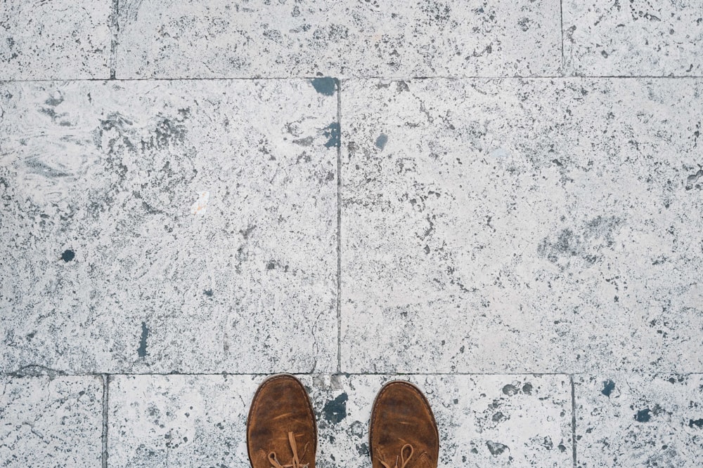 회색 콘크리트 바닥에 서 있는 갈색 신발을 신은 사람