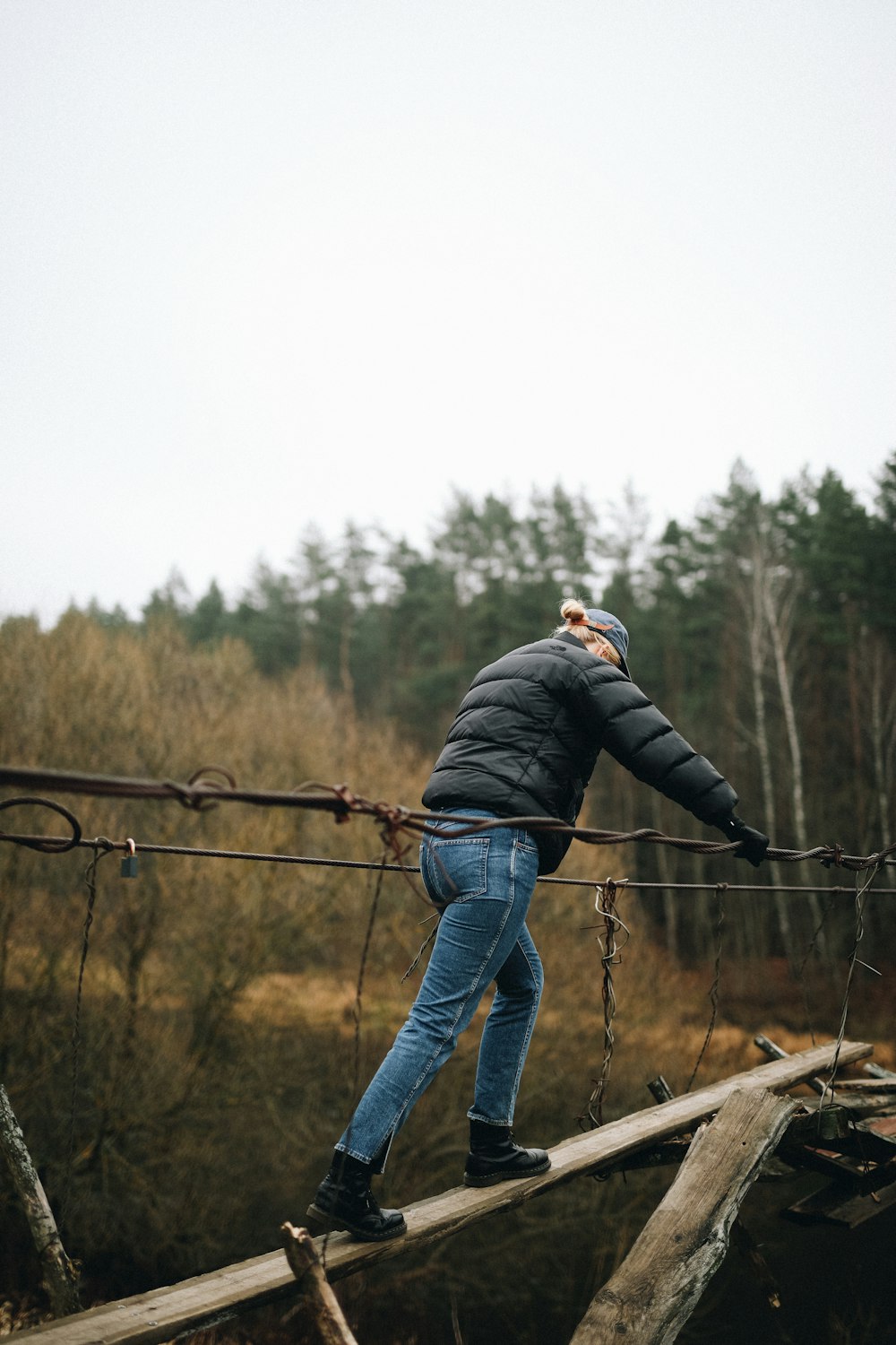 man in black jacket and blue denim jeans standing on brown wooden fence during daytime