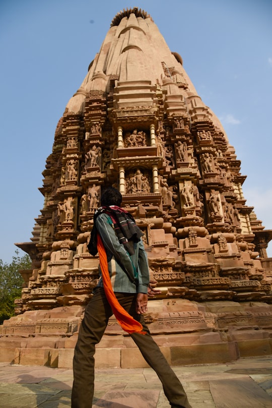 man in blue jacket and orange backpack standing in front of brown concrete building during daytime in Khajuraho India