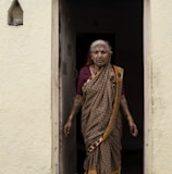 woman in yellow and brown sari standing beside white concrete wall during daytime