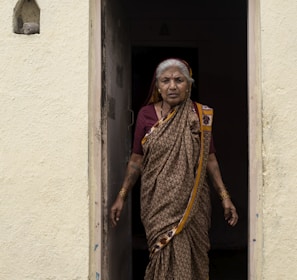 woman in yellow and brown sari standing beside white concrete wall during daytime