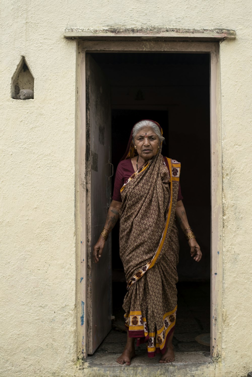 mulher em sari amarelo e marrom em pé ao lado da parede de concreto branco durante o dia
