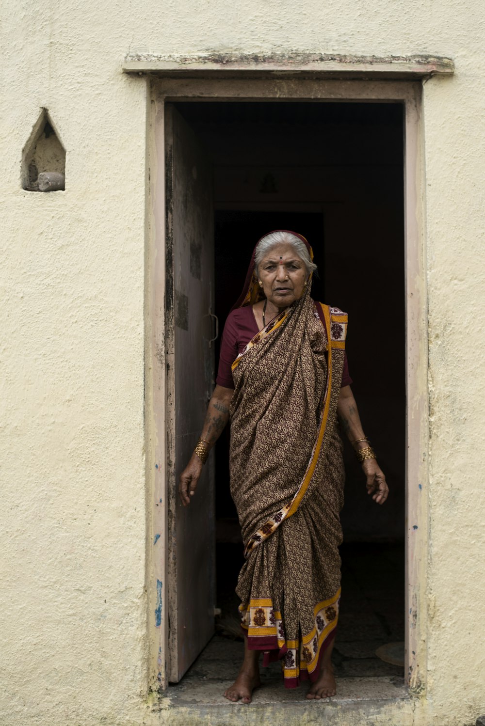 woman in yellow and brown sari standing beside white concrete wall during daytime