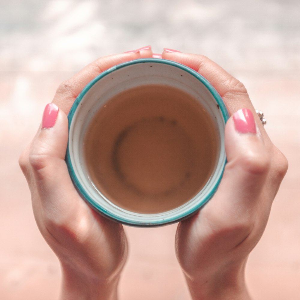 Persona sosteniendo una taza de cerámica azul con líquido marrón