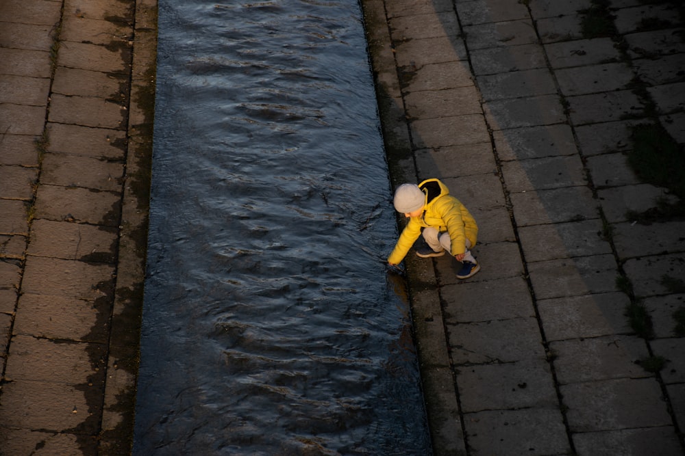 Niño en chaqueta amarilla y pantalones azules caminando en la acera durante el día