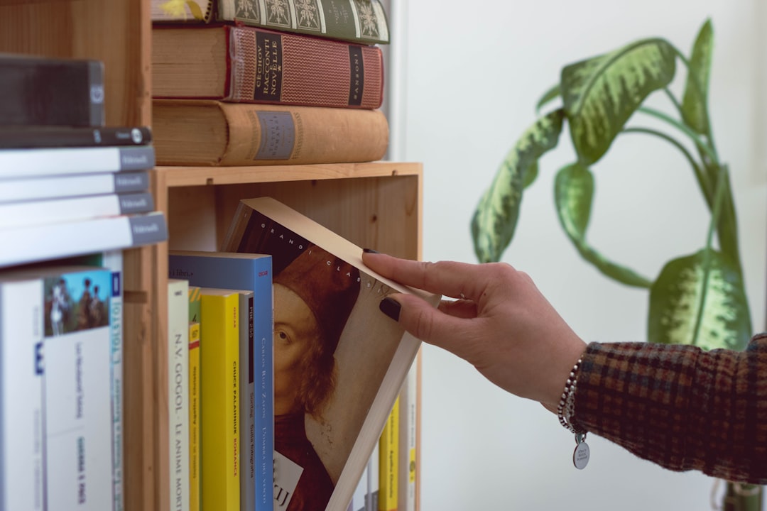 person holding book on book shelf