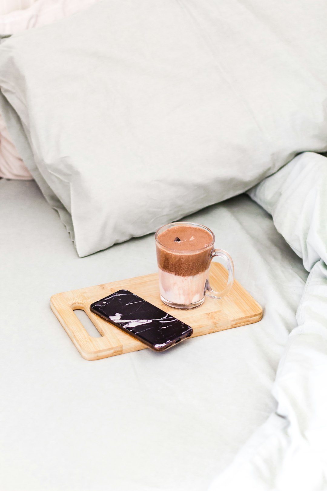 black iphone 5 on brown wooden tray beside clear glass mug on white textile