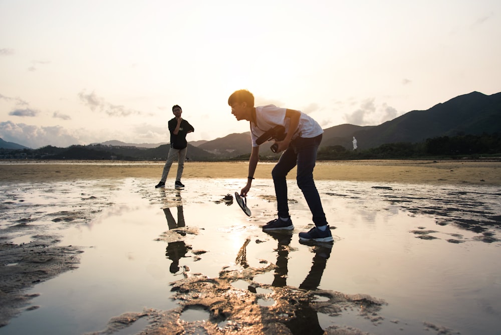 man in white shirt and black pants holding woman in white shirt on body of water