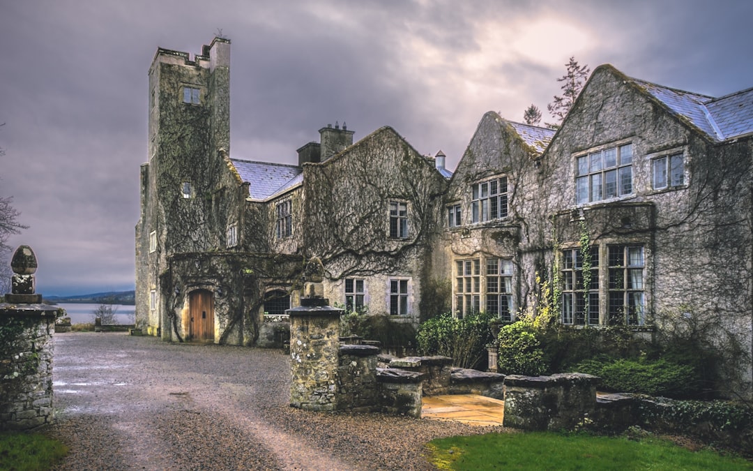 brown and gray concrete building under gray sky, A defoliated-ivy-clad Belle Isle Castle on Lough Erne during a brief re