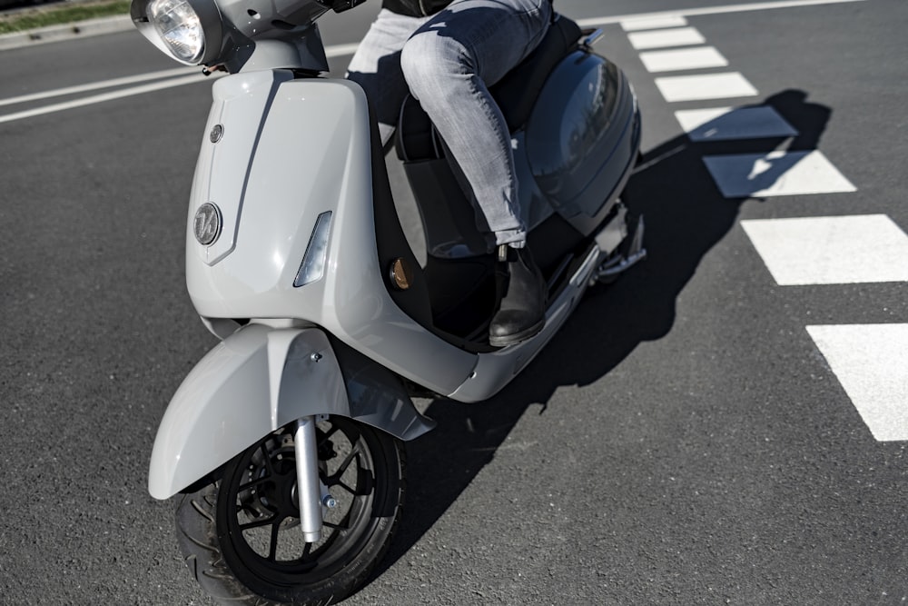 Personne en jean bleu et chaussettes noires chevauchant un scooter blanc et bleu