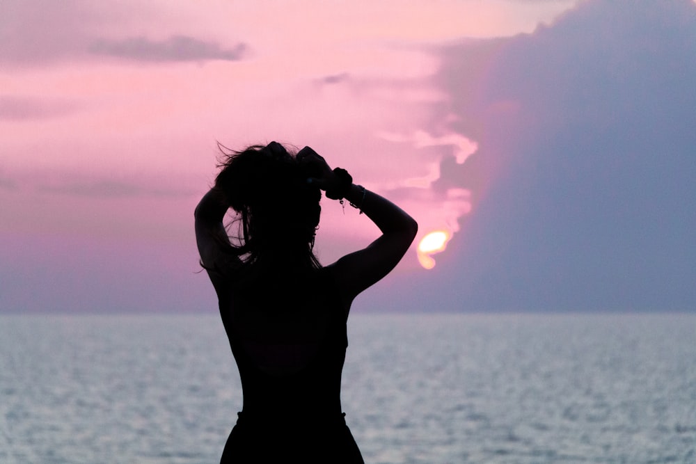 silhouette of woman standing near body of water during sunset