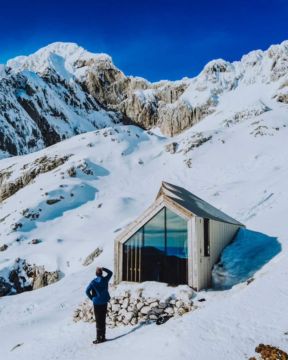 person in black jacket and black pants standing on snow covered ground near brown wooden house