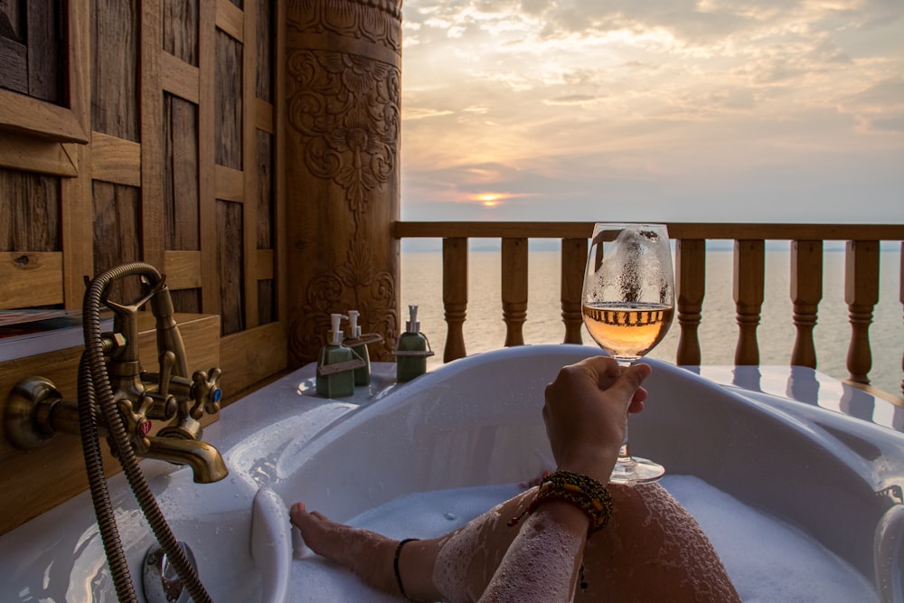 person in bathtub holding wine glass