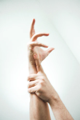 Sensual, artistic photograph capturing intertwined hands, glistening with subtle gold accents, set within a dark immersive environment.
