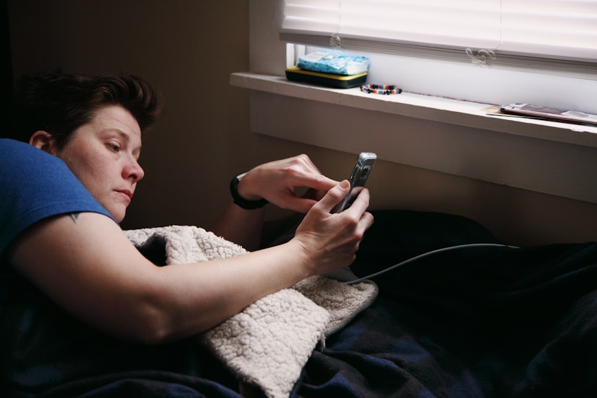 seorang pemuda sedang bermain handphone di kasur ketika remote working.