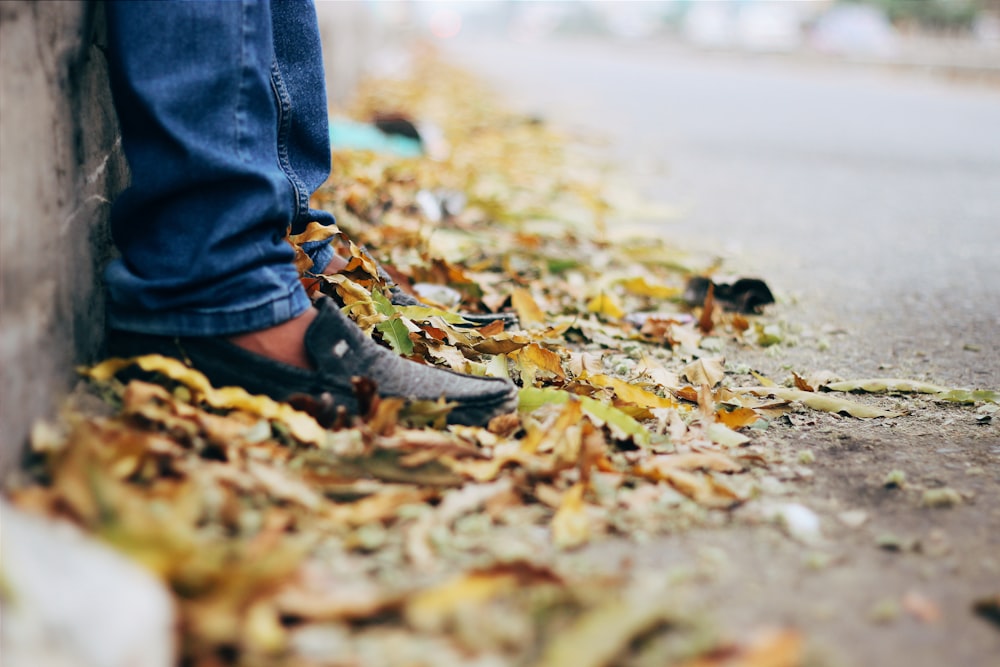 persona in jeans blu denim e stivali di pelle marrone in piedi su foglie secche marroni sul vicino su su su