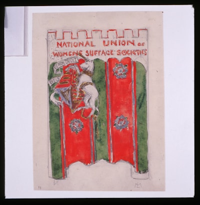 A banner featuring a medieval-style shield and coat of arms with a lion holding a flag. The banner has a red and green background, and the text at the top reads 'NATIONAL UNION OF WOMEN'S SUFFRAGE SOCIETIES.' The top edge of the banner is crenellated, resembling a castle wall.
