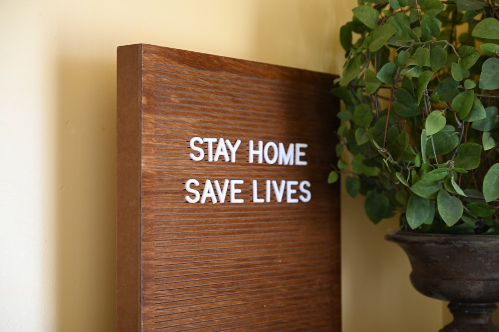 a wooden sign that says stay home save lives next to a potted plant