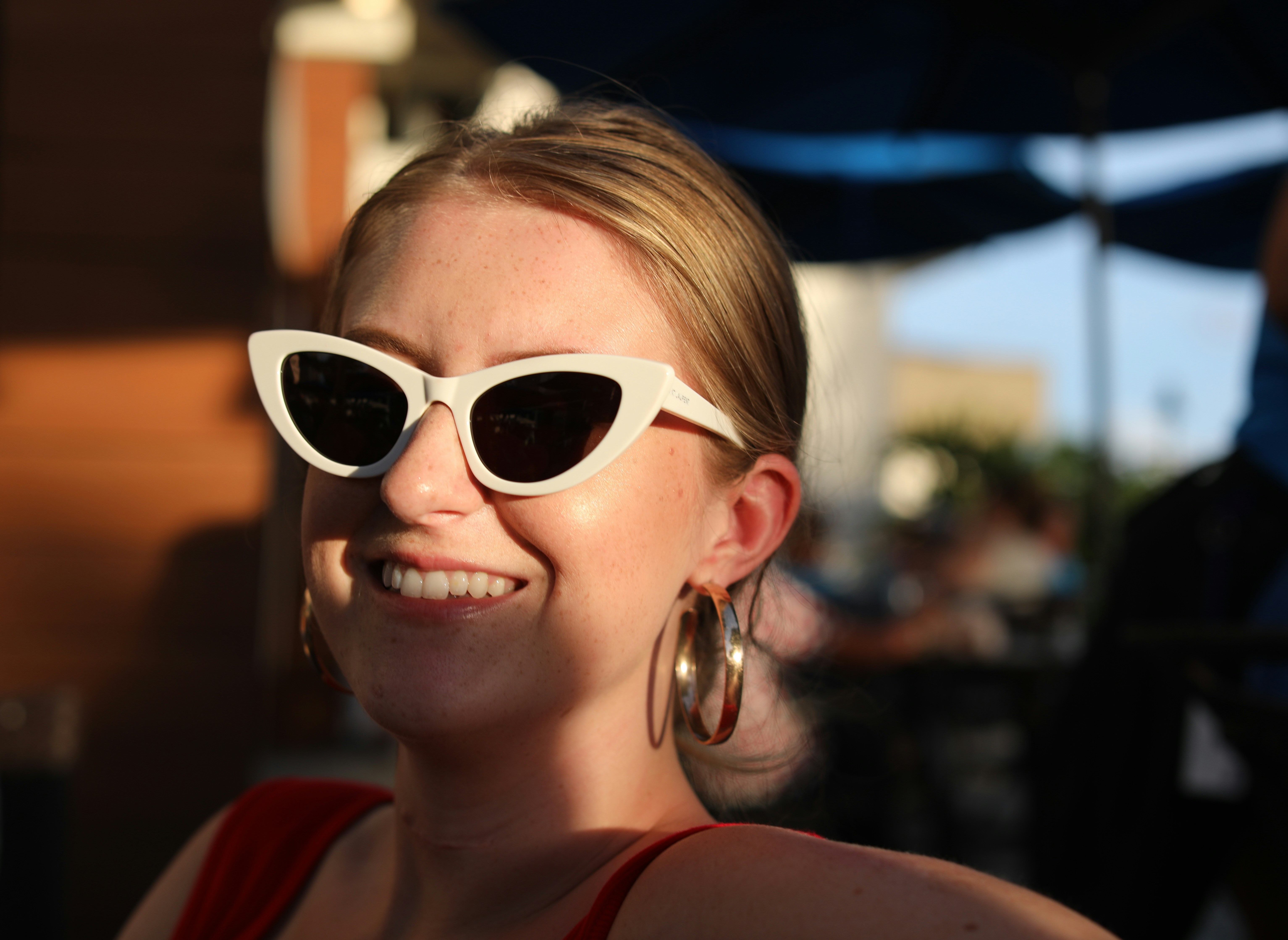 woman in red tank top wearing white framed sunglasses, Young woman laughing during golden hour. 