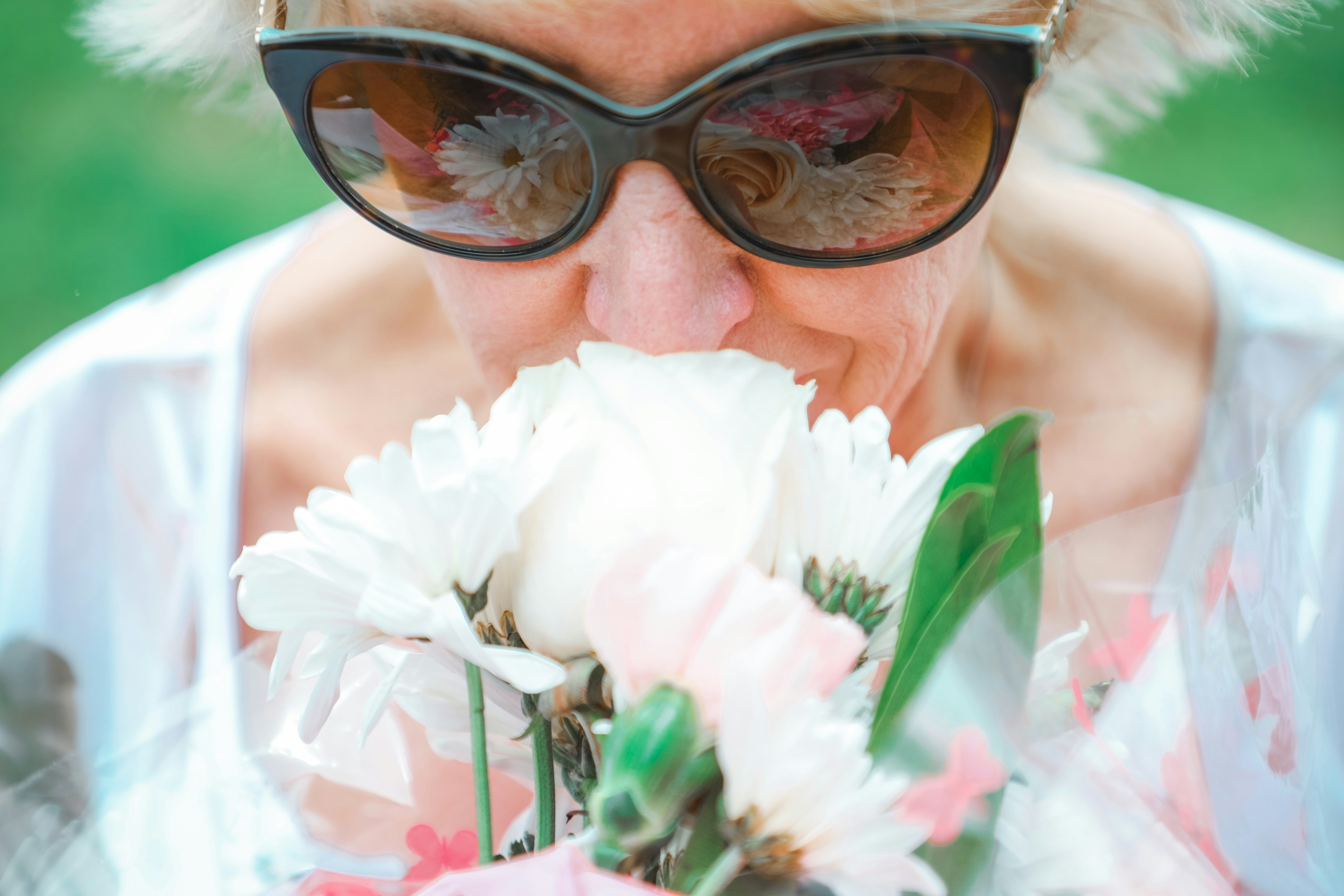 woman in black framed sunglasses holding white flower, Women stopping to smell the flowers. 
