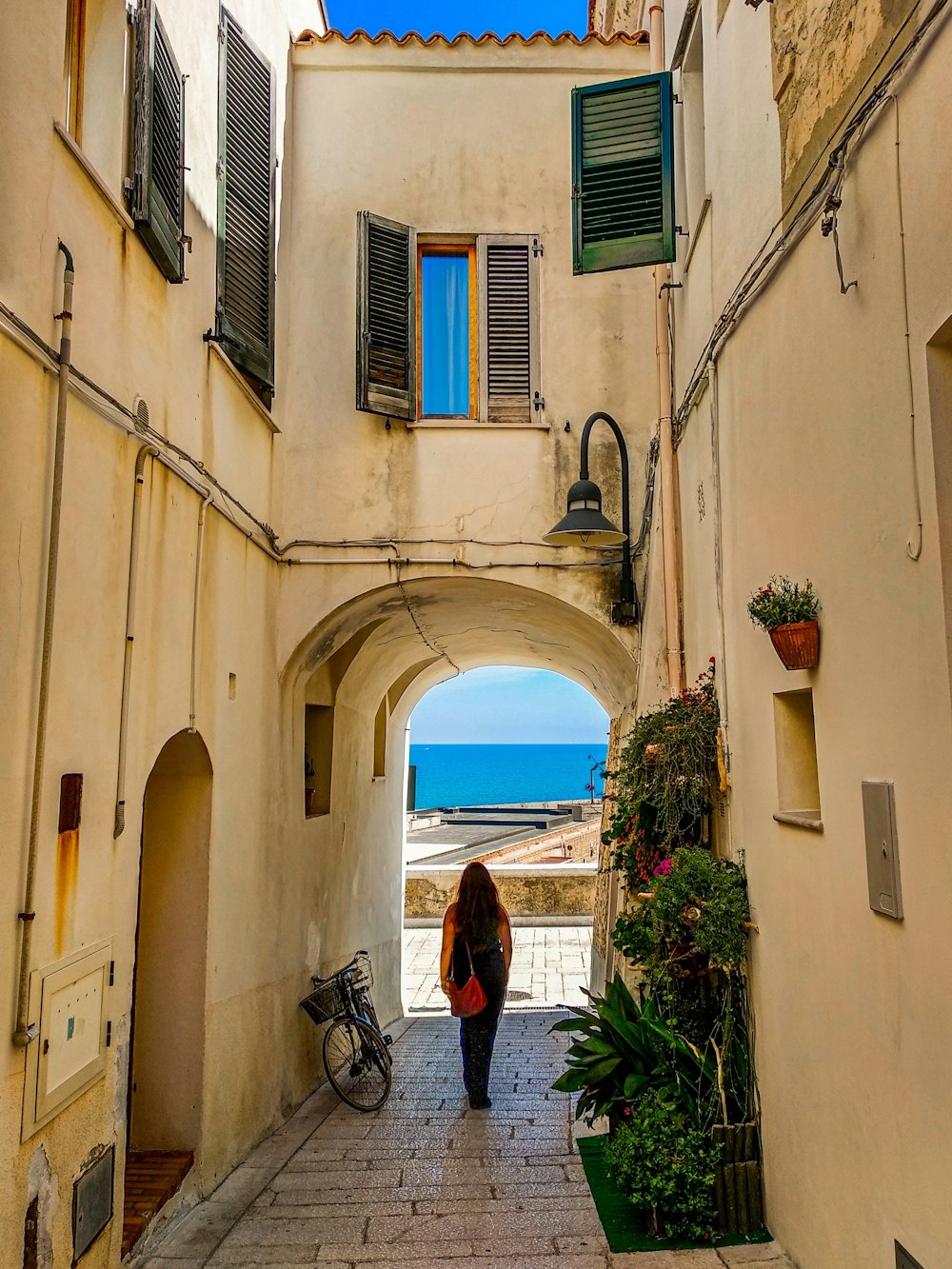 donna in giacca nera e pantaloni neri in piedi davanti all'edificio in cemento bianco durante il giorno