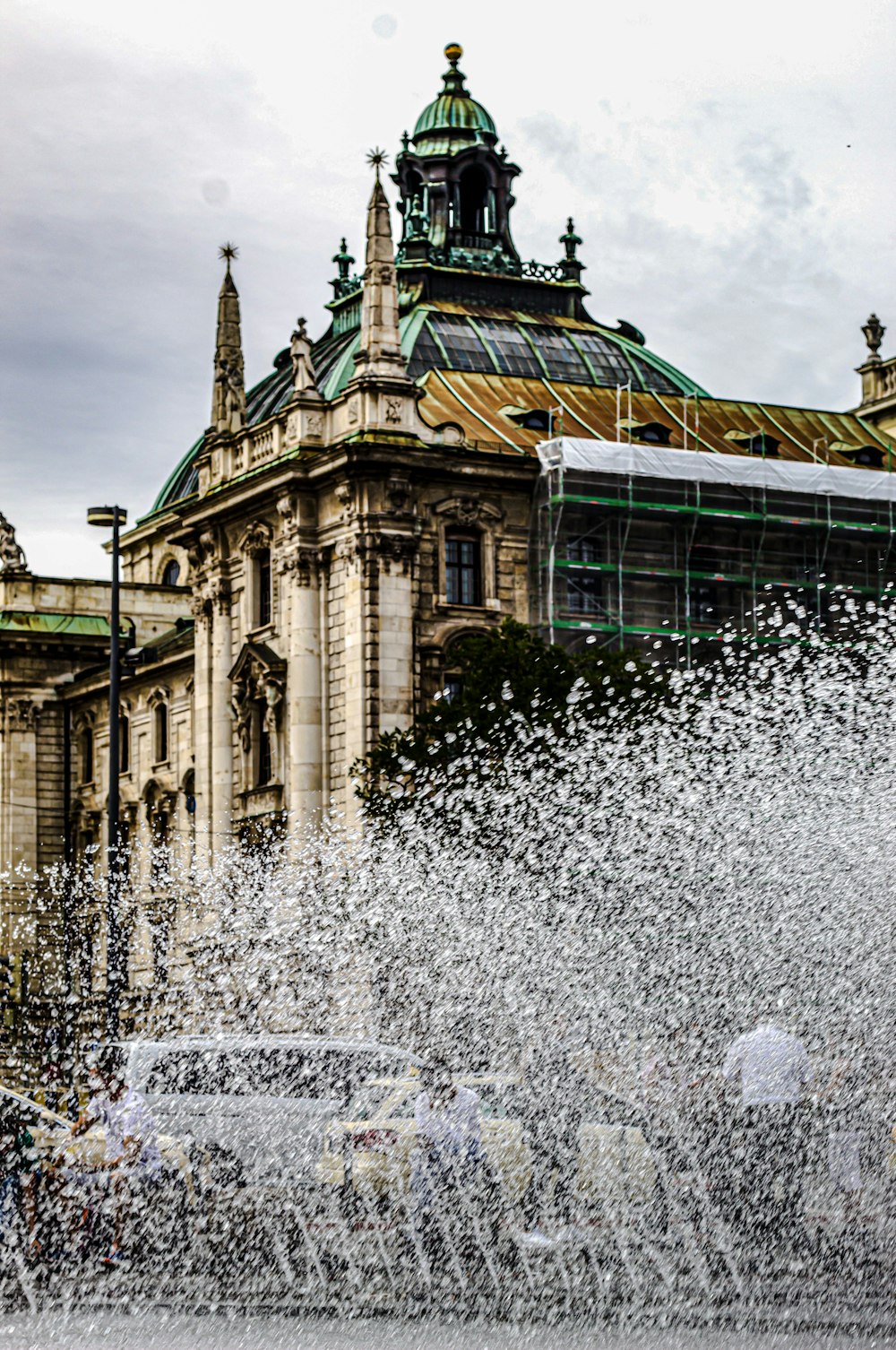 Wasserfontäne vor grün-braunem Gebäude