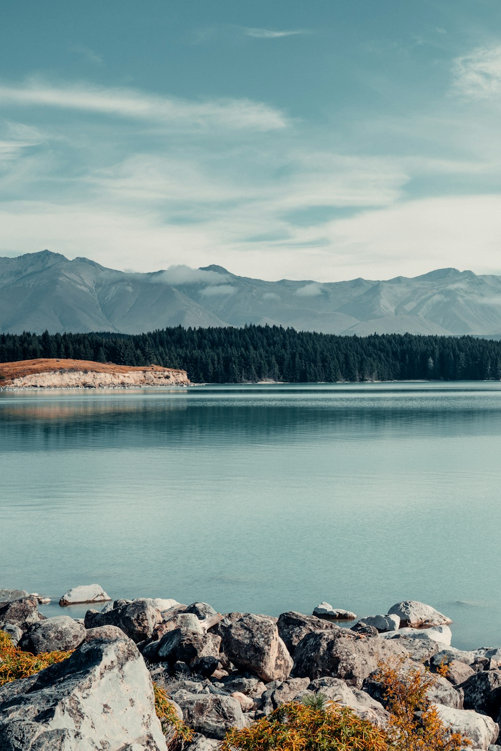 lake near trees and mountains under cloudy sky during daytime