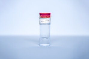 A clear glass vial with a red cap is centered in the image. A label on the vial reads '2019-NCOV'. The background is a soft gradient of blue, giving it a sterile and clinical atmosphere.