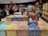 A bustling candy store with a colorful display of individually wrapped chocolates arranged in open bins. Shoppers are selecting candies from the wide variety, while others browse the shelves filled with sweet treats. The store has a warm and inviting atmosphere.
